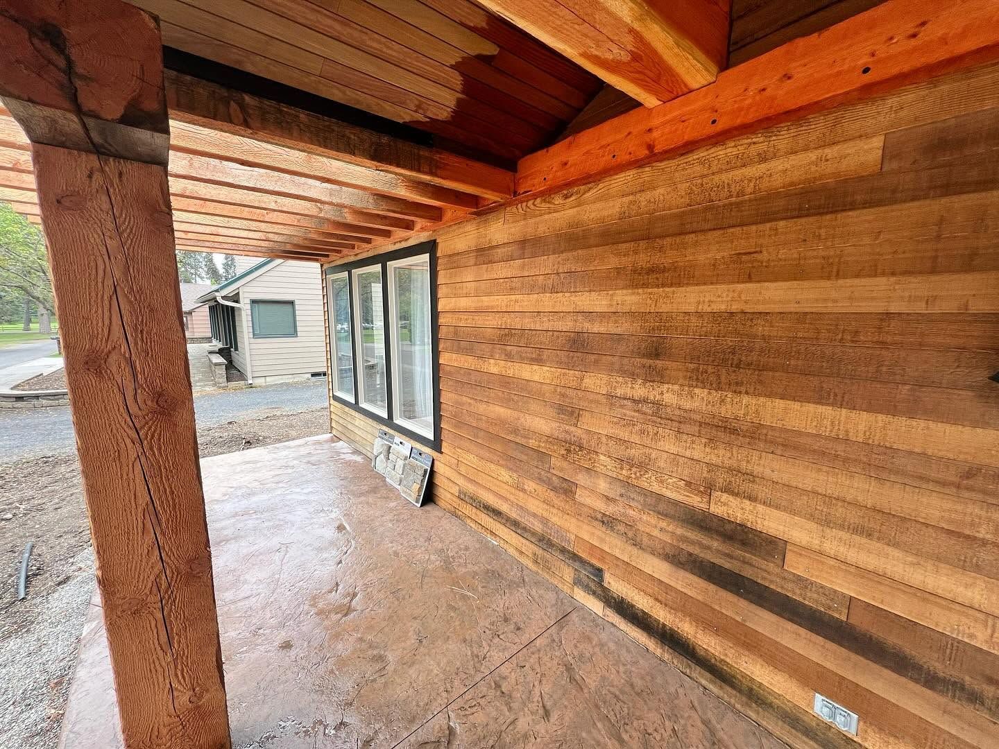 Wood-paneled covered porch with exposed beams and windows, overlooking a gravel drive and RV.