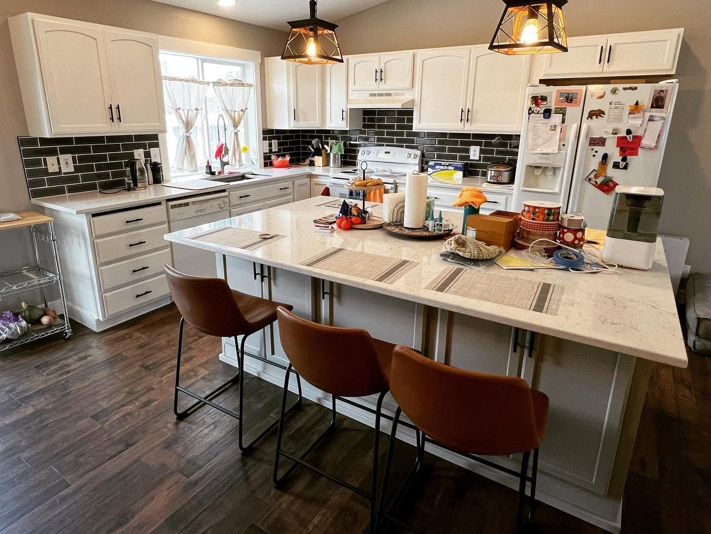 Bright modern kitchen with white cabinets, a central island, and three brown stools on dark wood flooring