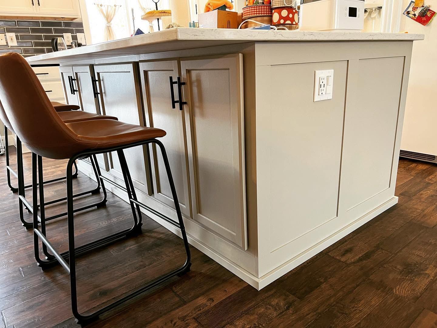 Kitchen island with white paneling and a brown barstool on a dark wood floor
