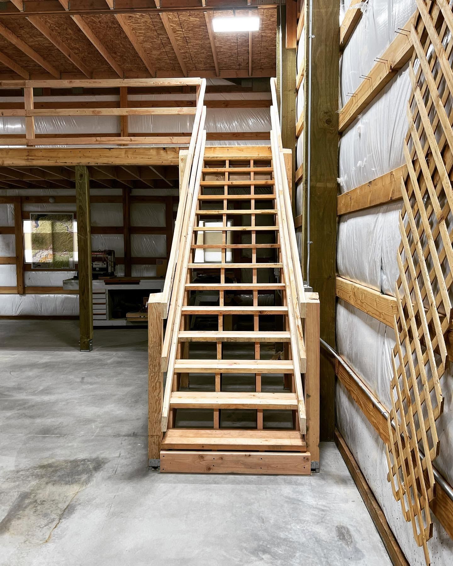Wooden indoor staircase in an unfinished basement with concrete floor and exposed wall insulation