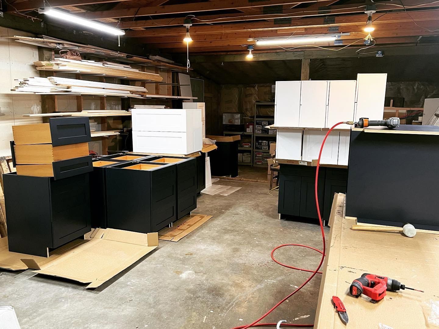 Warehouse with stacked white cabinets and black counters, red cords on the floor, and tools on a workbench.