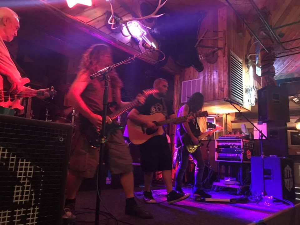 Band performing live on stage under red and purple lights in a wooden-paneled venue.