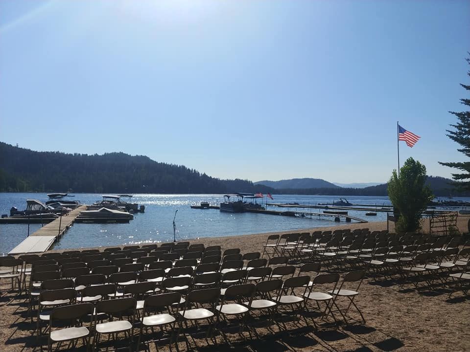 Rows of chairs face a lake with docks and boats, mountains in the distance, and an American flag.