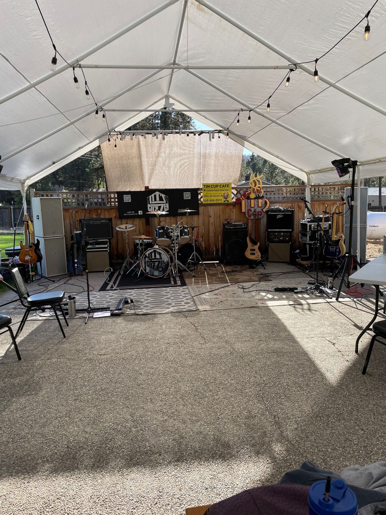 Band setup under a white tent, with drums, amps, and guitars on a stage.