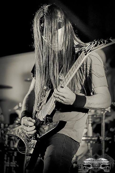 Guitarist playing electric guitar on stage, long hair obscuring face. Black and white photo.