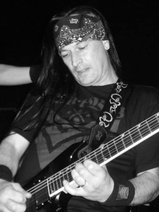 Guitarist playing electric guitar on stage, wearing a bandana and wristband.