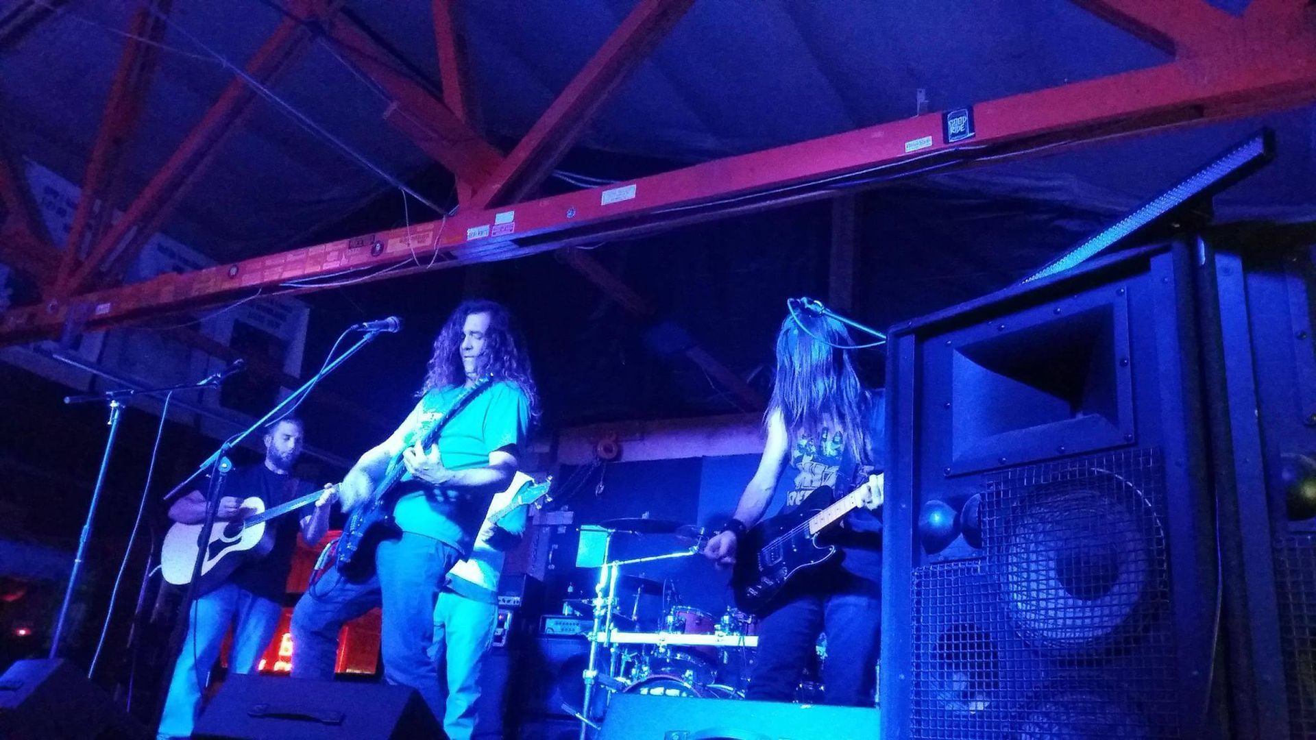 Band playing on stage under blue lights; guitarist, bassist, drummer, singer.