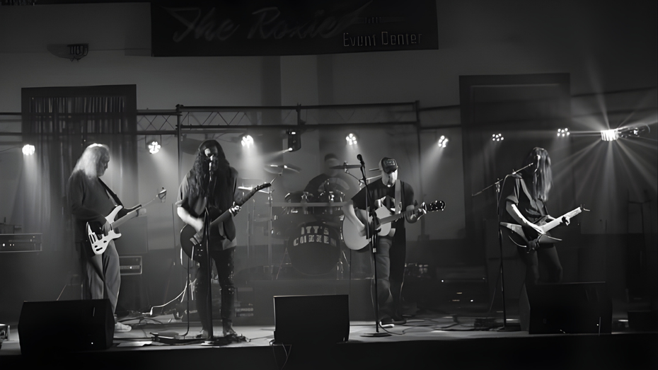 Band performing on stage, playing instruments under stage lighting; black and white.