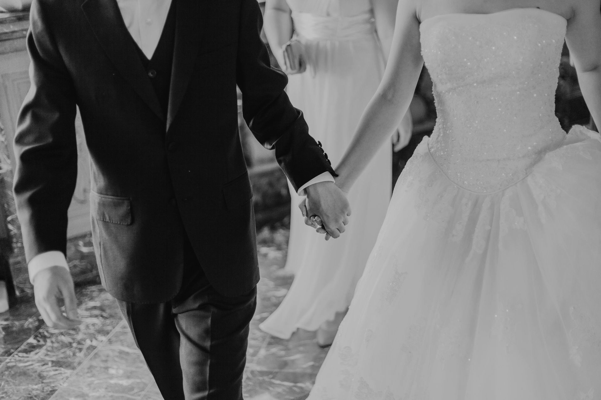 Couple in formal attire, holding hands, walking. Bride in a gown, groom in a suit. Wedding setting.