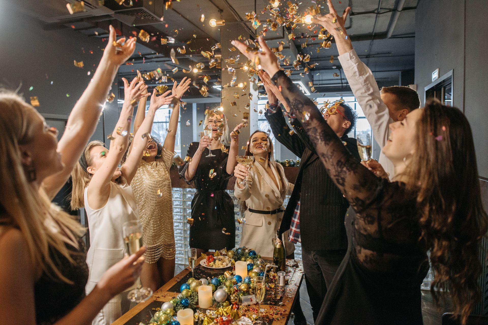 People celebrating indoors, raising hands as confetti sparkles above a decorated table.