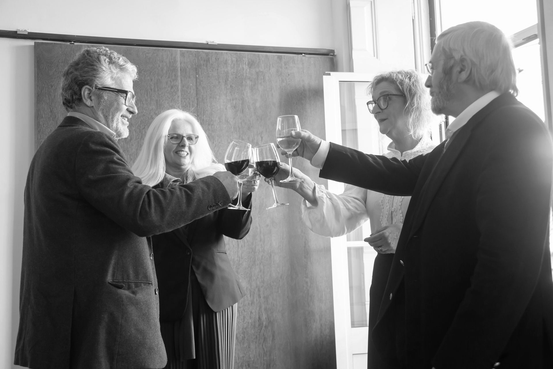 Four people toasting with wine glasses in a well-lit room, black and white.
