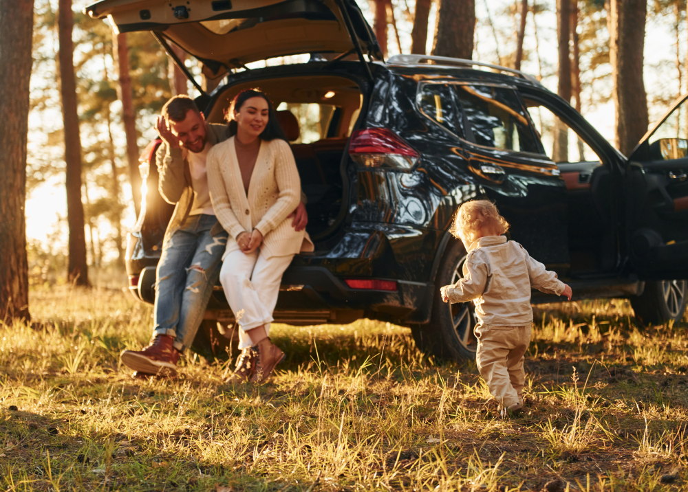 A family is sitting in the back of a car in the woods.