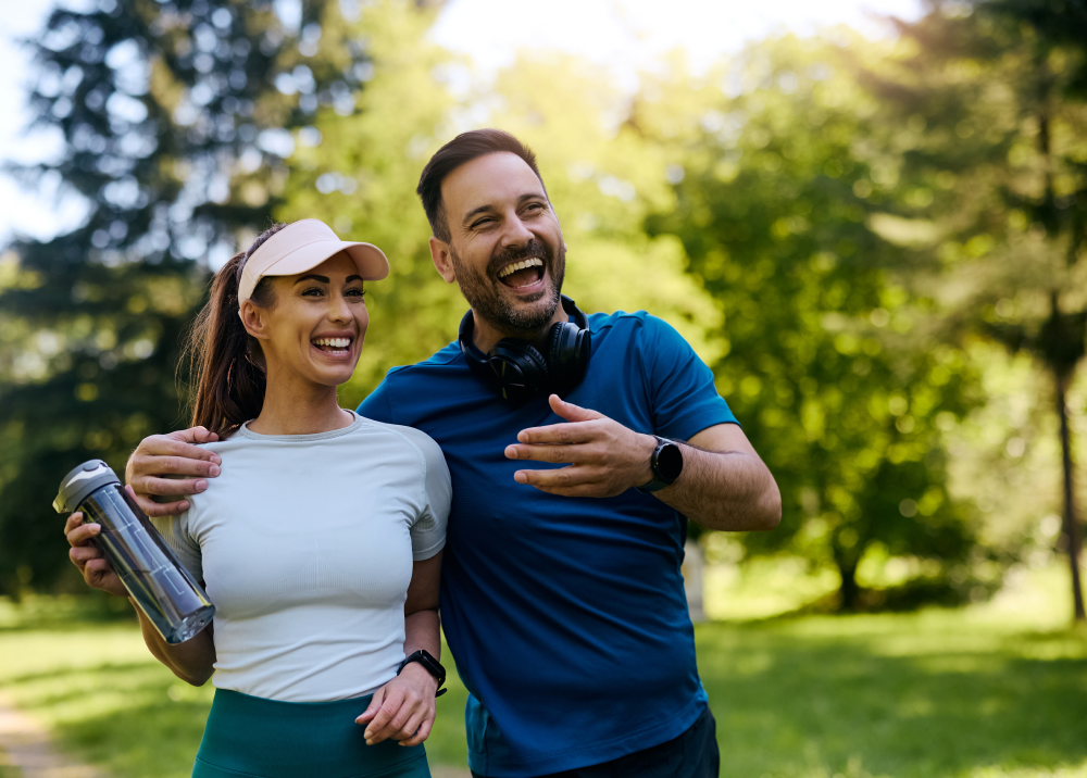 A man and a woman are laughing while walking in a park.