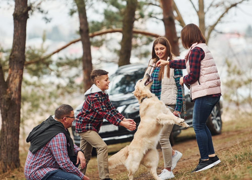 A family is playing with a dog in front of a car.