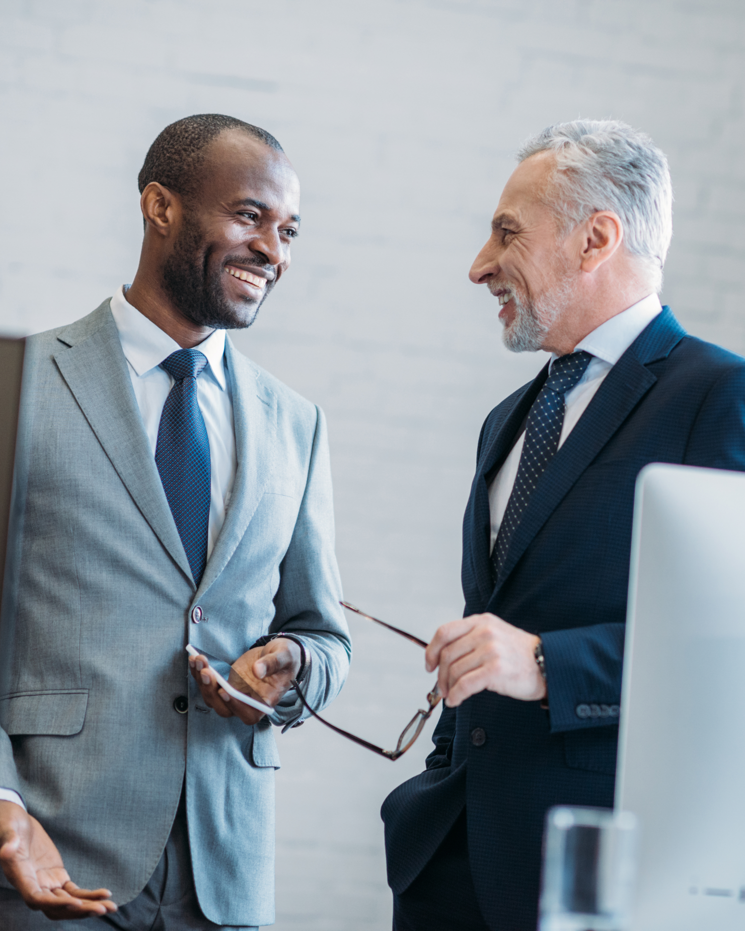 Two men in suits and ties are talking to each other in an office.