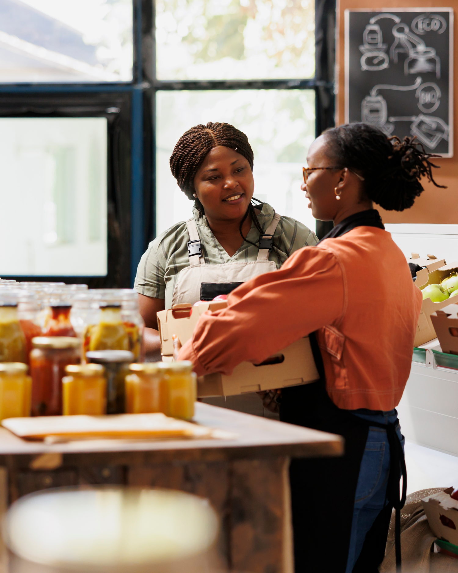Two women are working in a kitchen and one is holding a box
