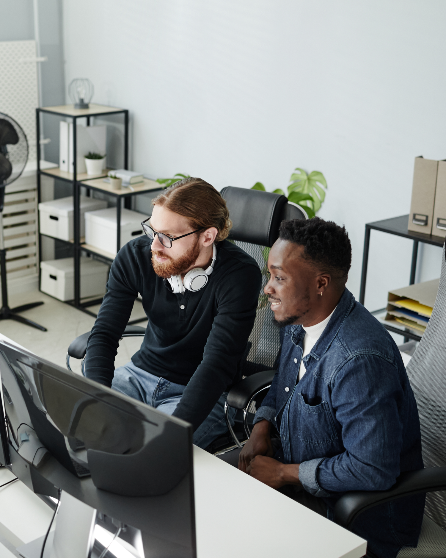 Two men are sitting at a desk looking at a computer screen.