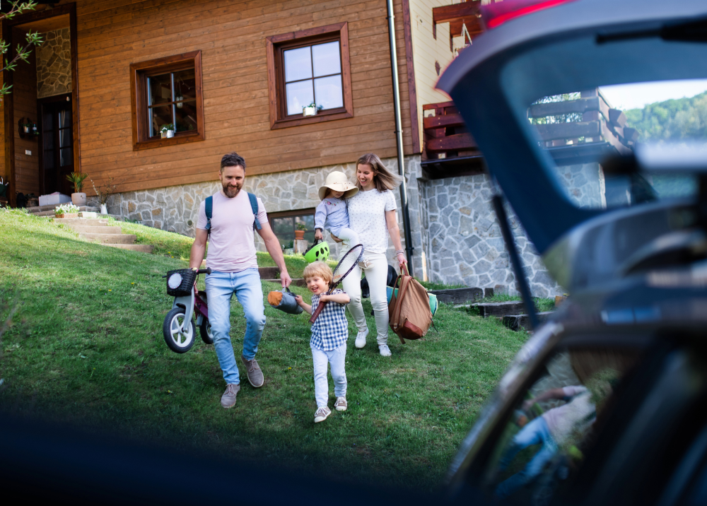 A family is walking towards a house with a car trunk open.