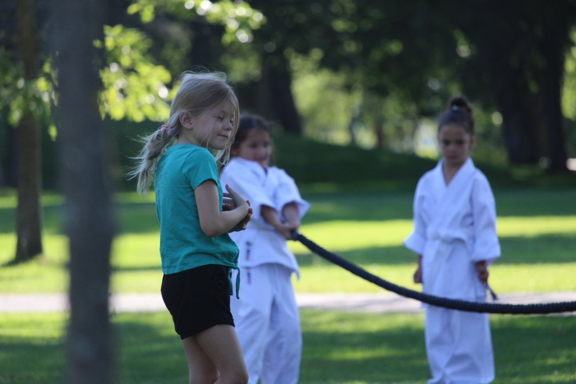 A group of young girls are playing with a rope in a park.