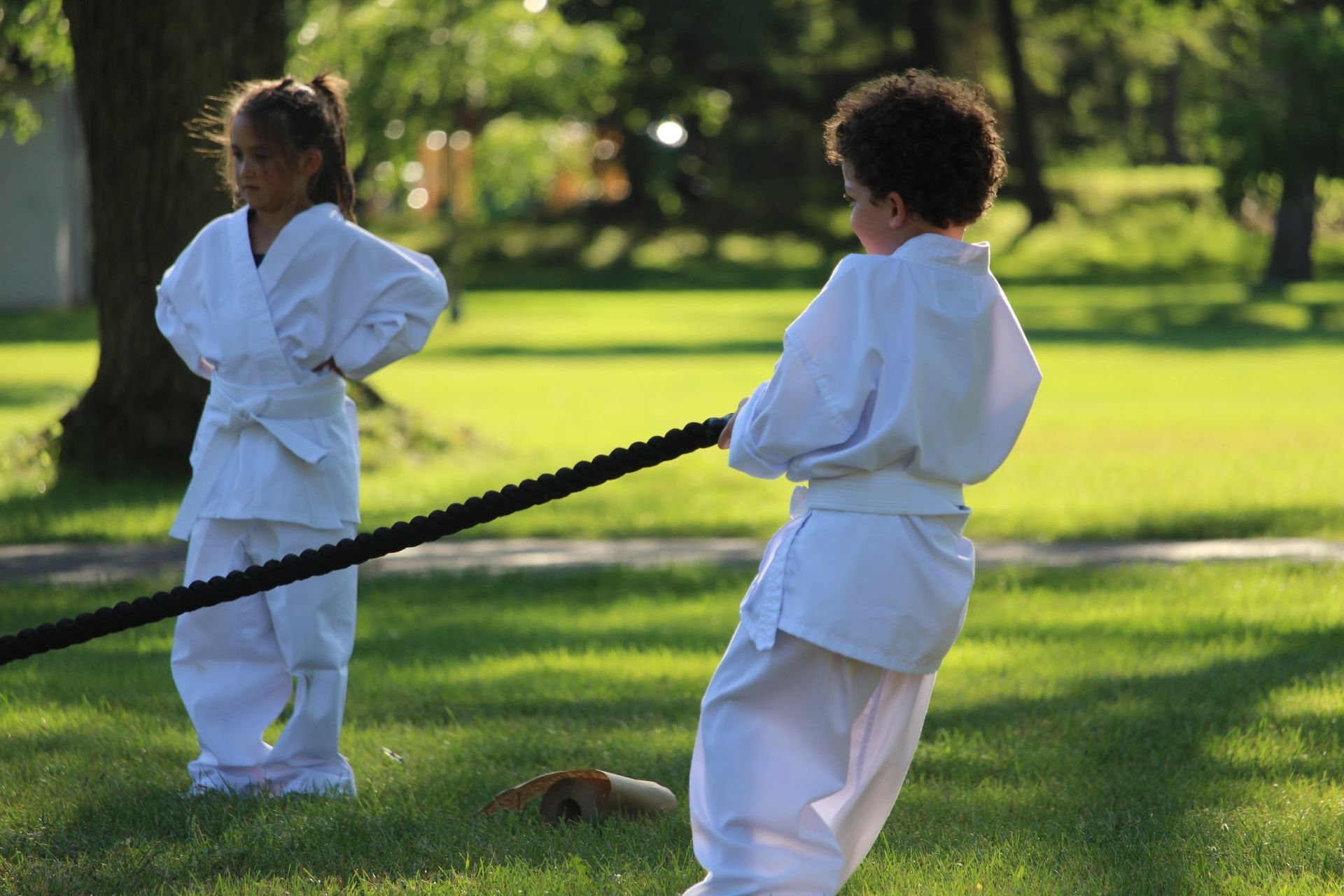 A boy and a girl are pulling a rope in a park.