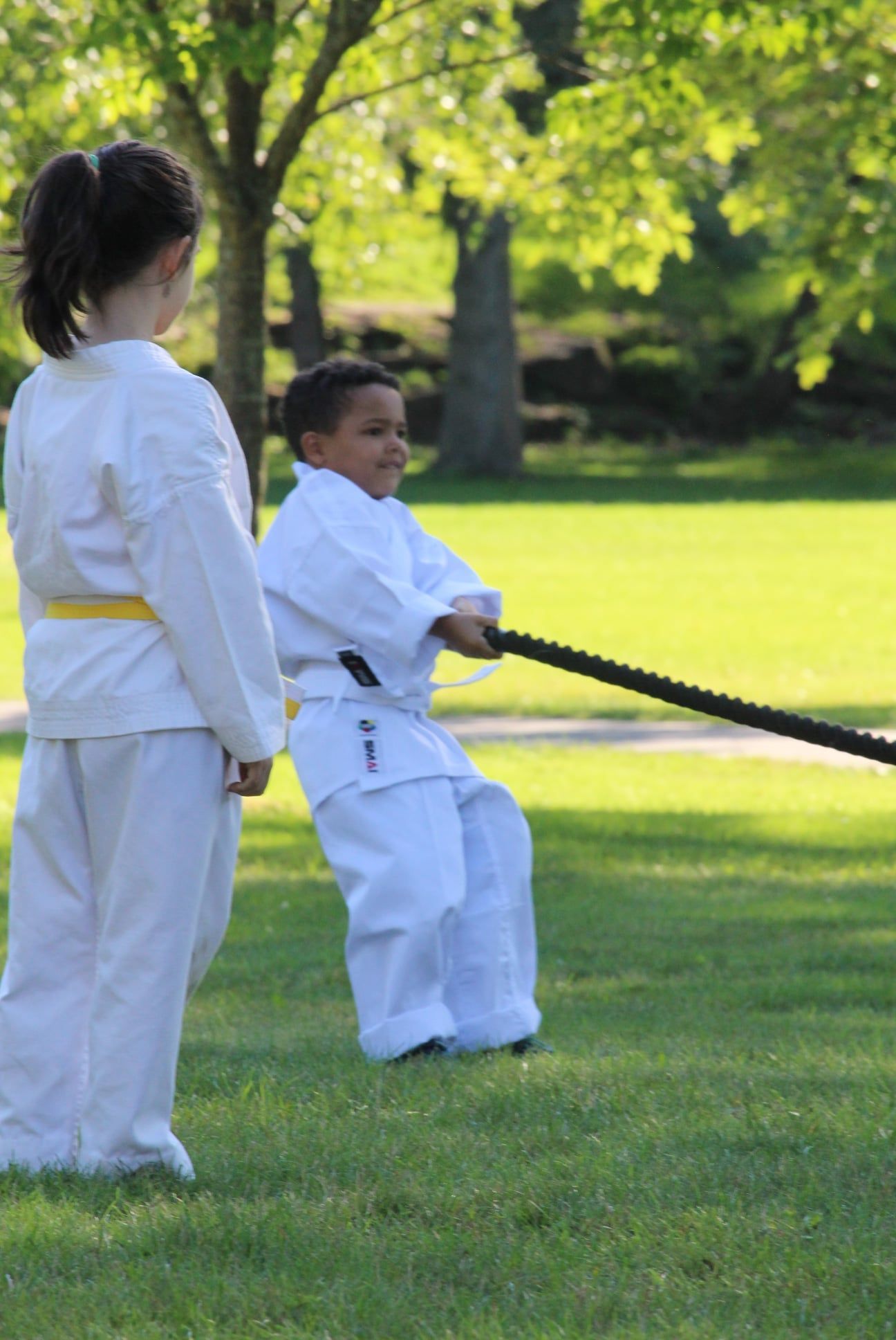 A boy and a girl are pulling a rope in a park.