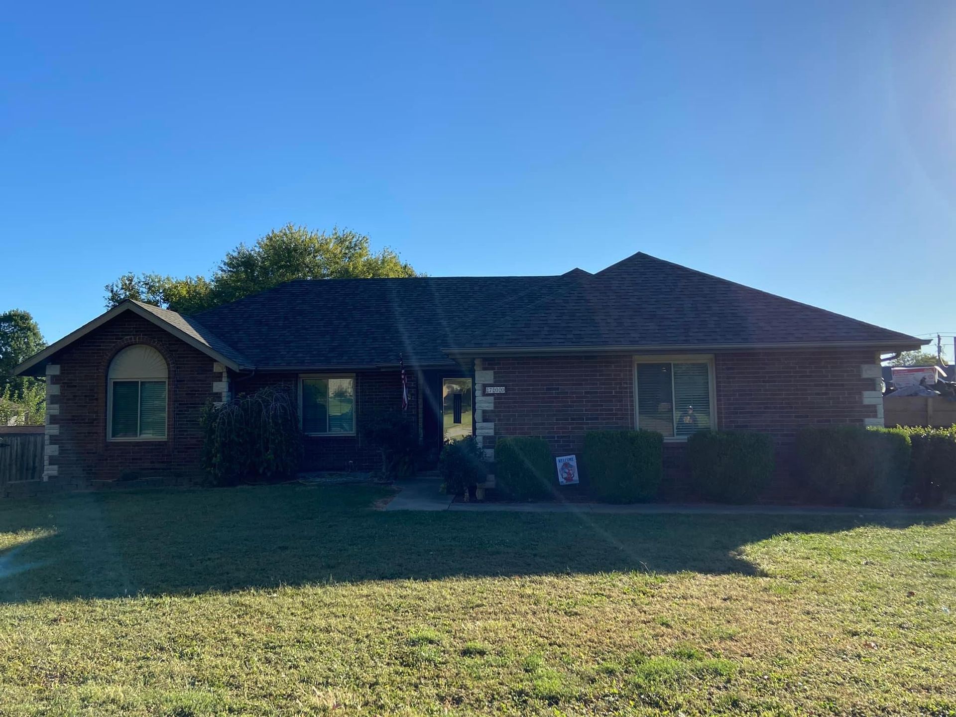 A brick house with a black roof is sitting on top of a lush green field.