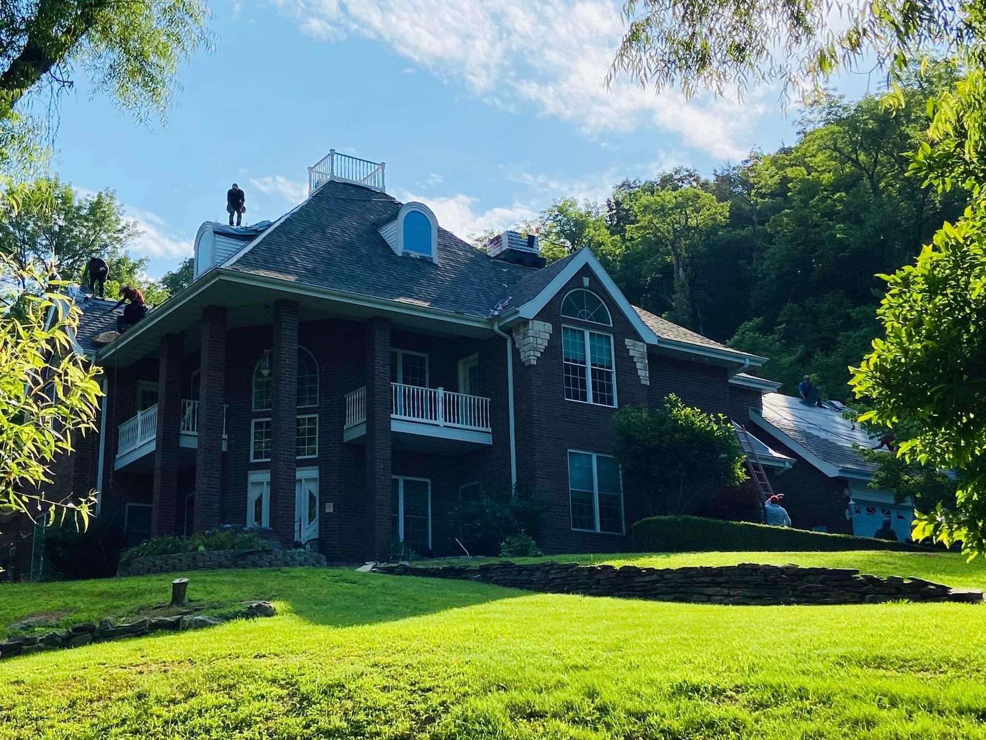 A large brick house is sitting on top of a lush green hillside.