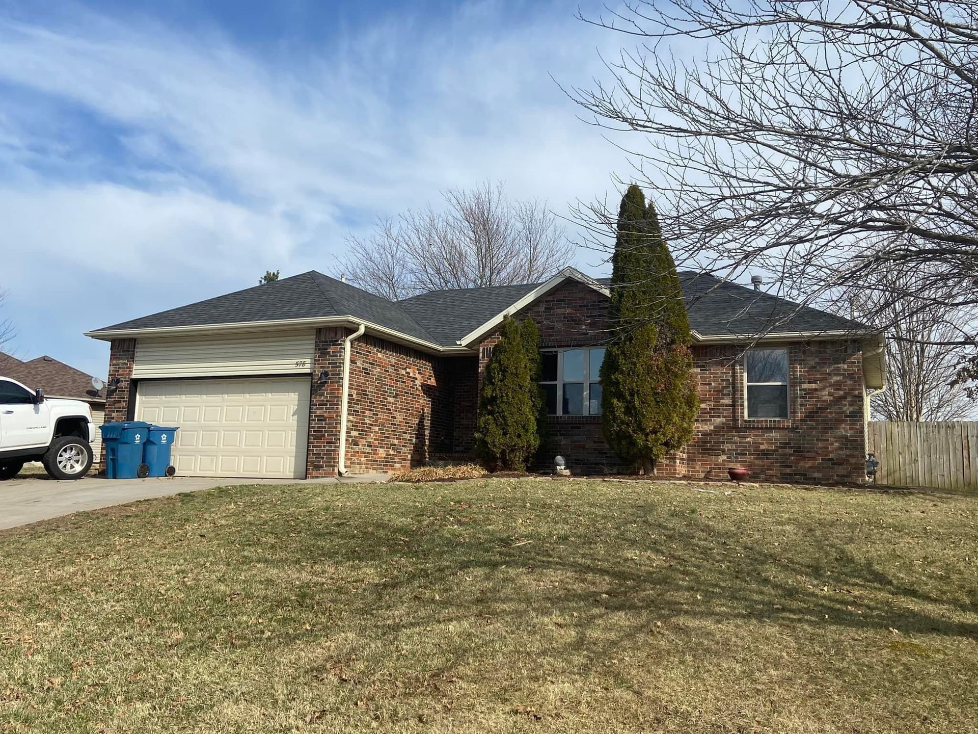 A white truck is parked in front of a brick house.