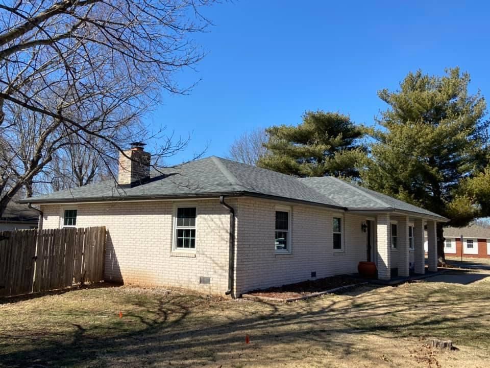A white brick house with a gray roof and a fence in front of it.