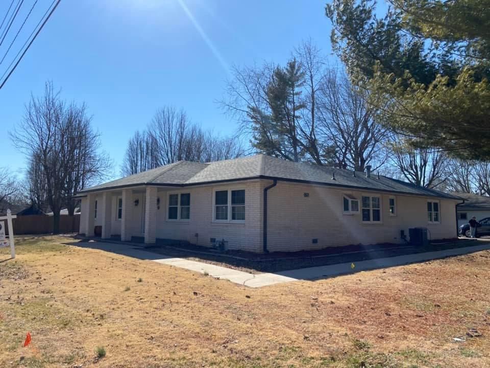 A white house with a gray roof is sitting in the middle of a grassy field.
