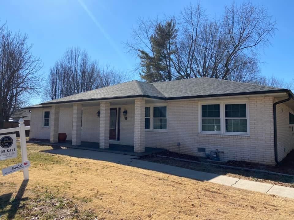 A white brick house with a for sale sign in front of it.