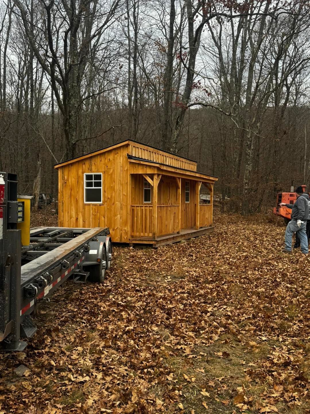 A wooden shed is being built on a trailer in the woods.