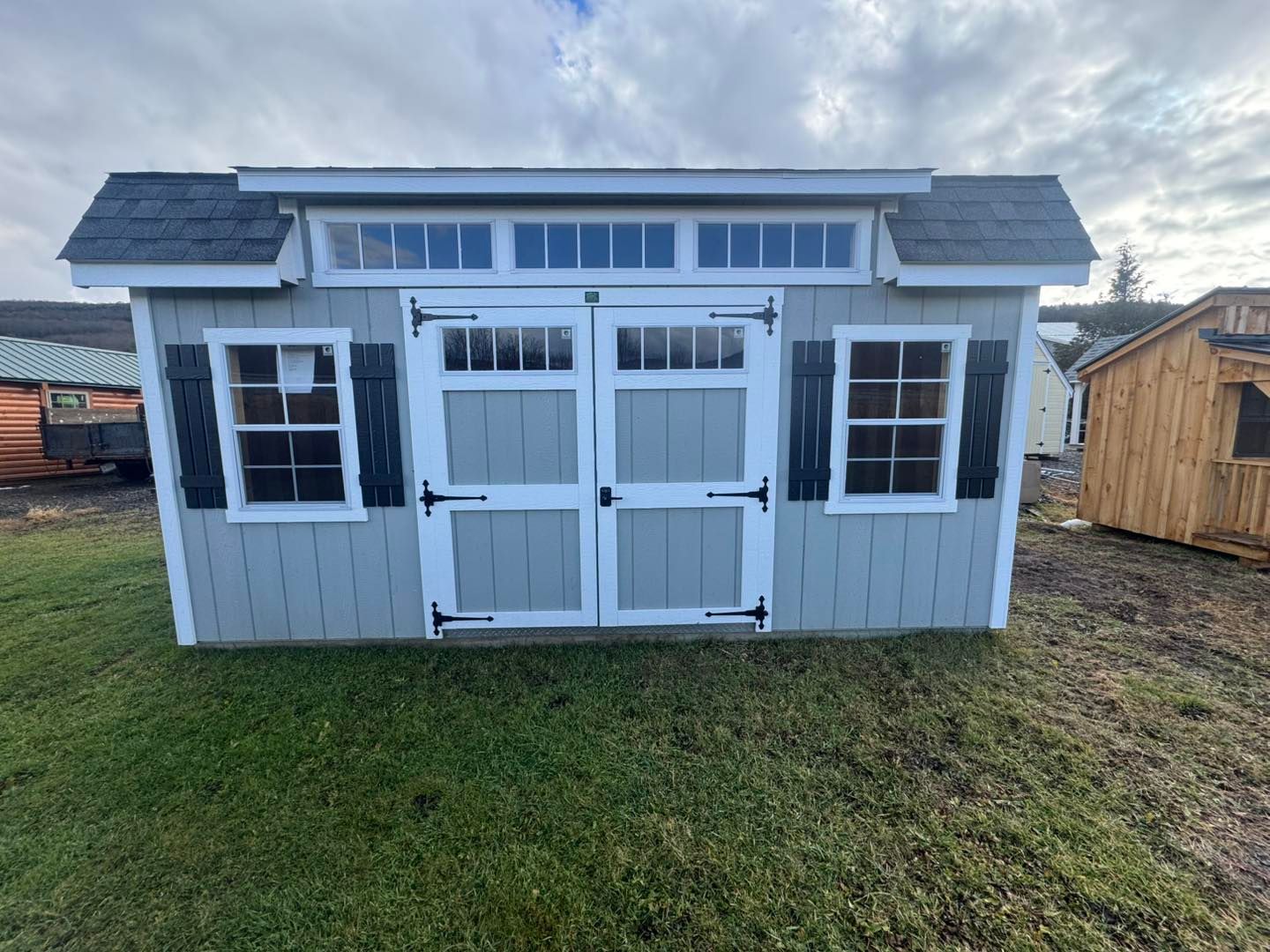 A gray shed with white trim and shutters is sitting on top of a lush green field.