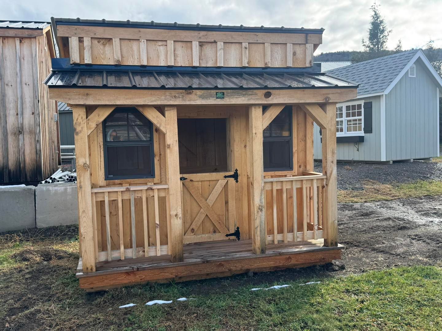 A small wooden shed with a screened in porch is sitting in the grass.
