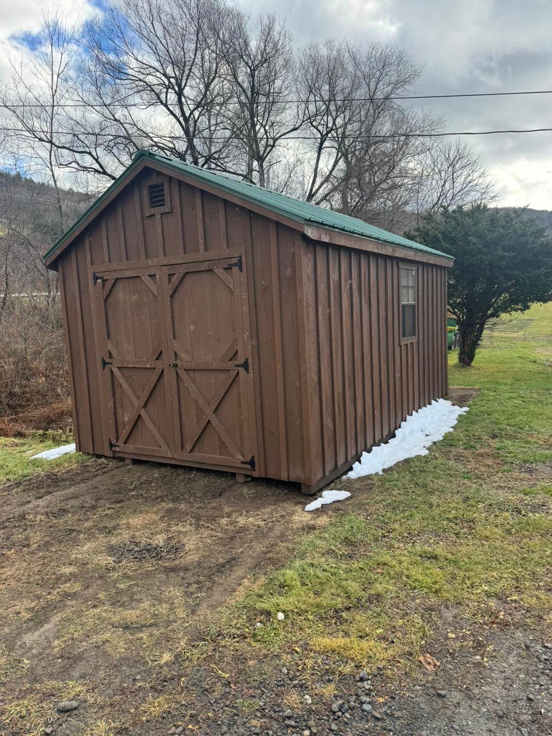A wooden shed with a green roof is sitting in the middle of a field.