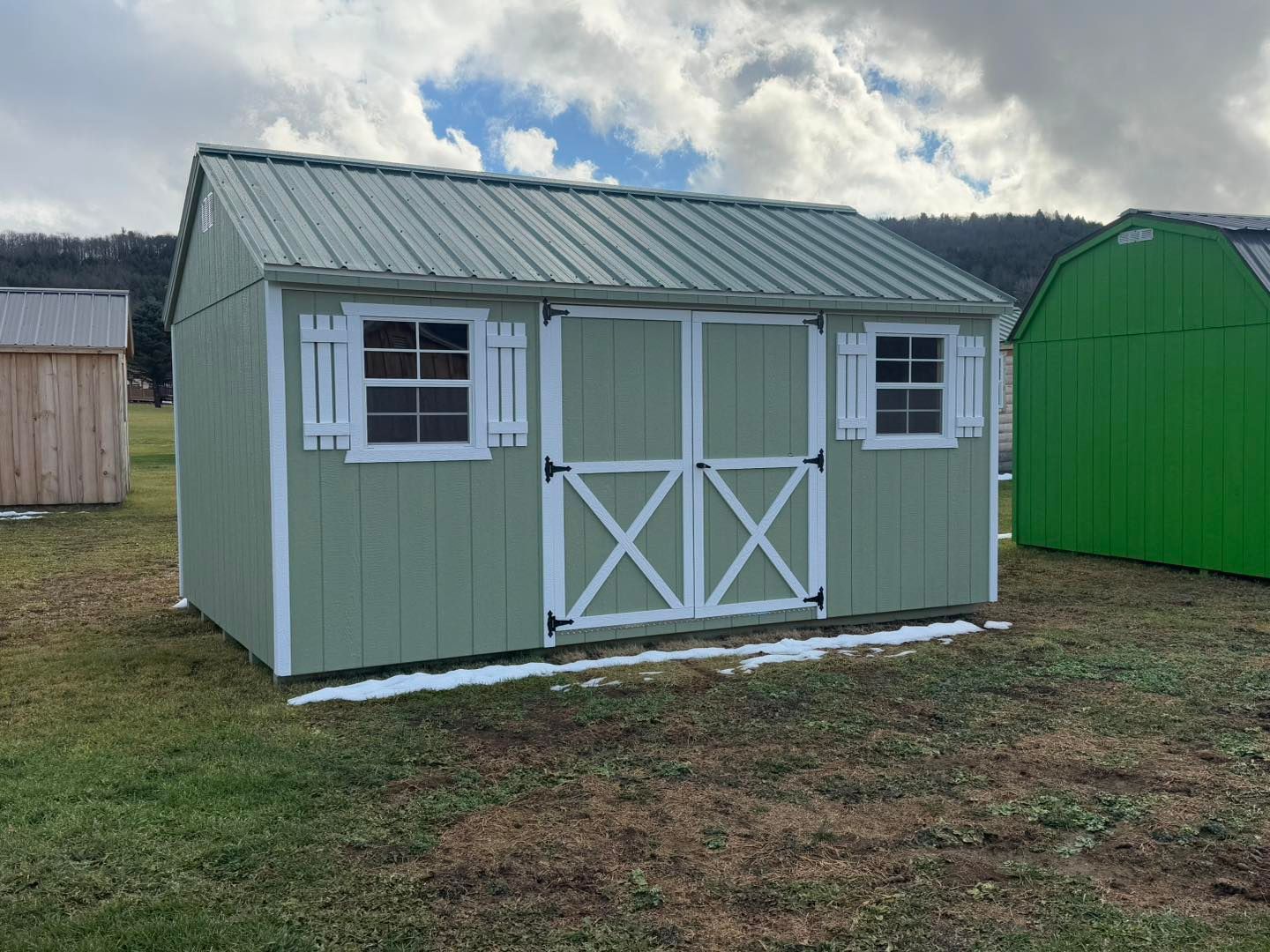 A green shed with white trim is sitting in the middle of a grassy field.