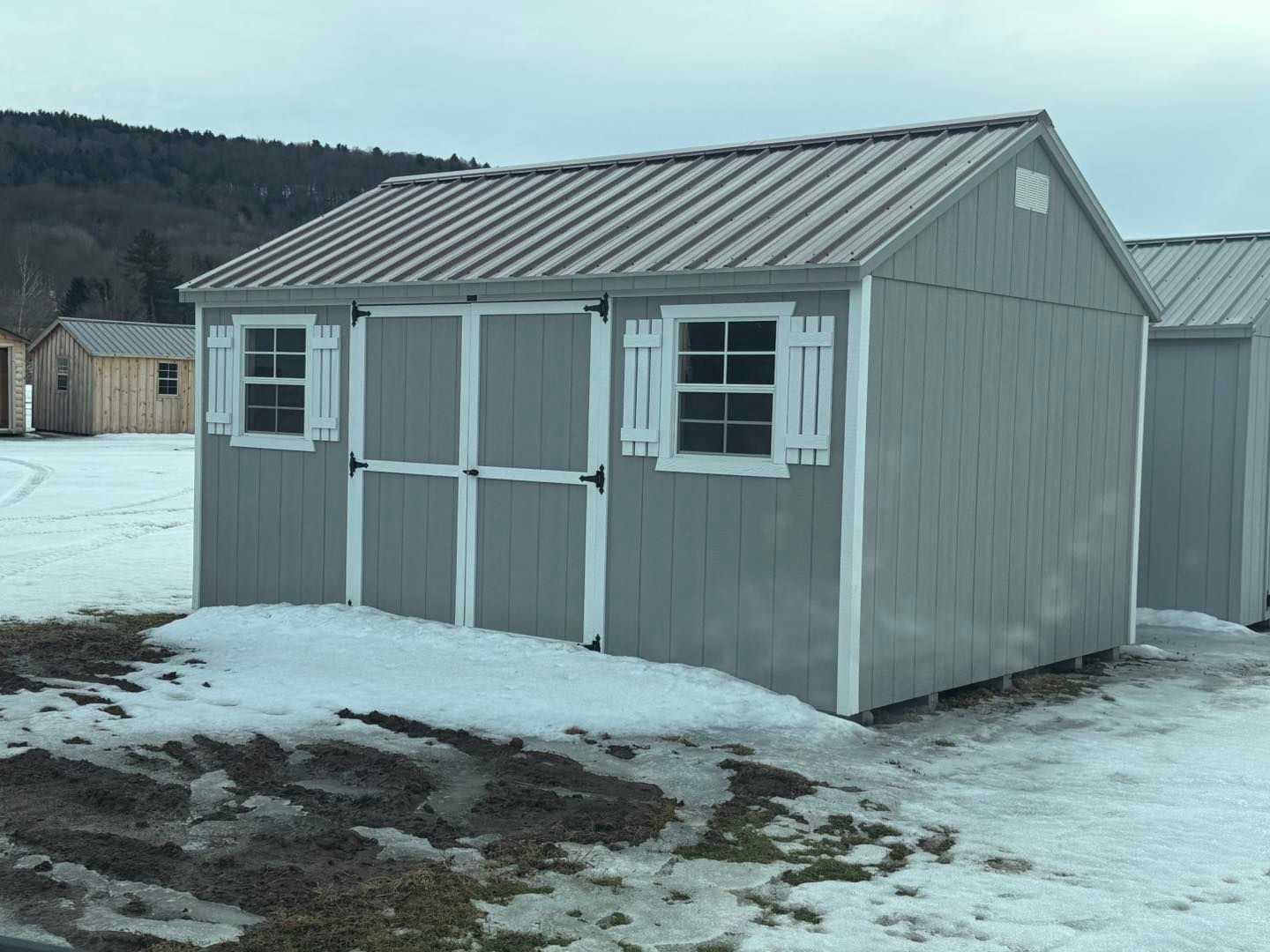 A gray shed with a metal roof is sitting in the snow.