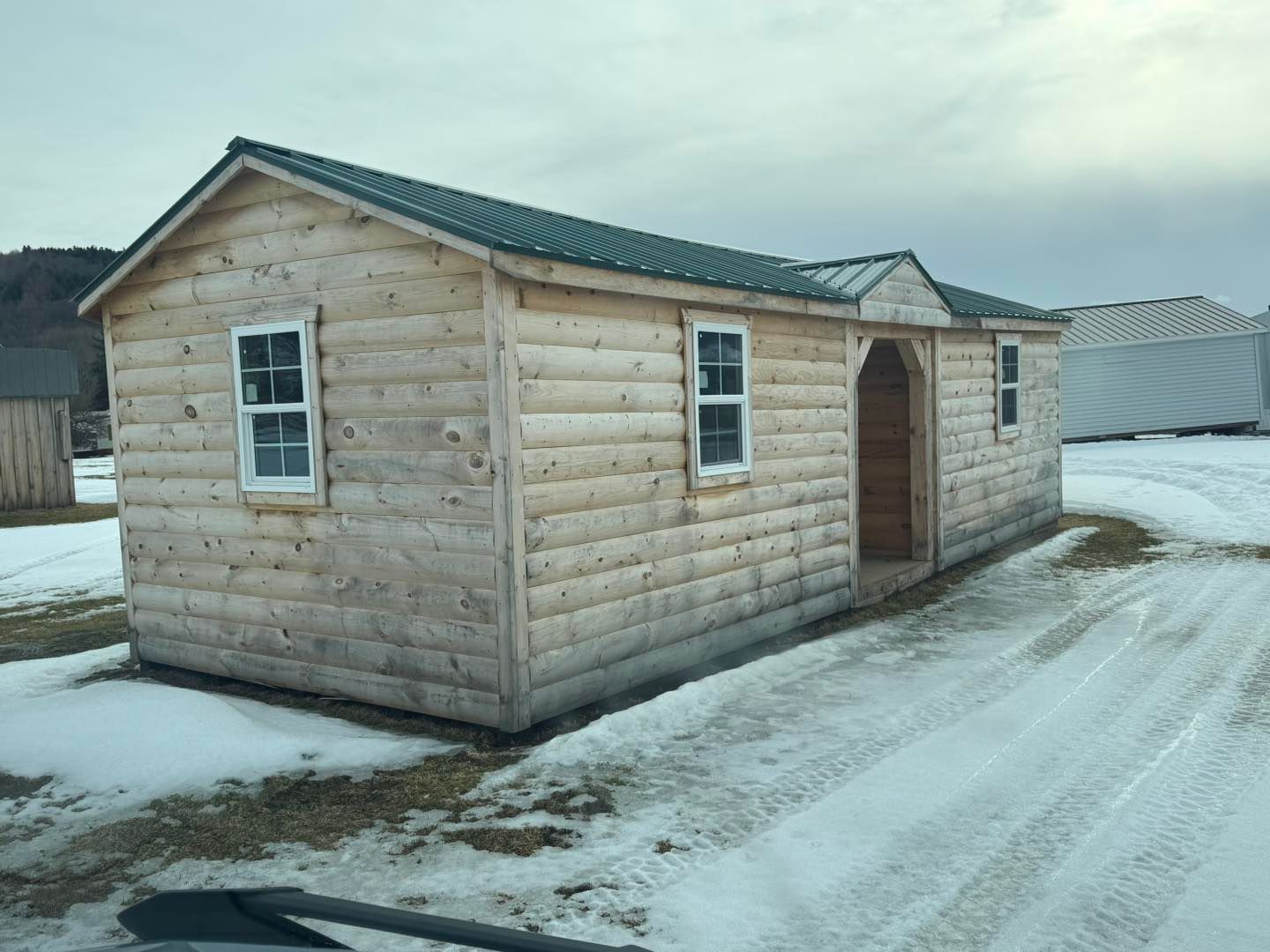 A small log cabin with a green roof is sitting in the snow.