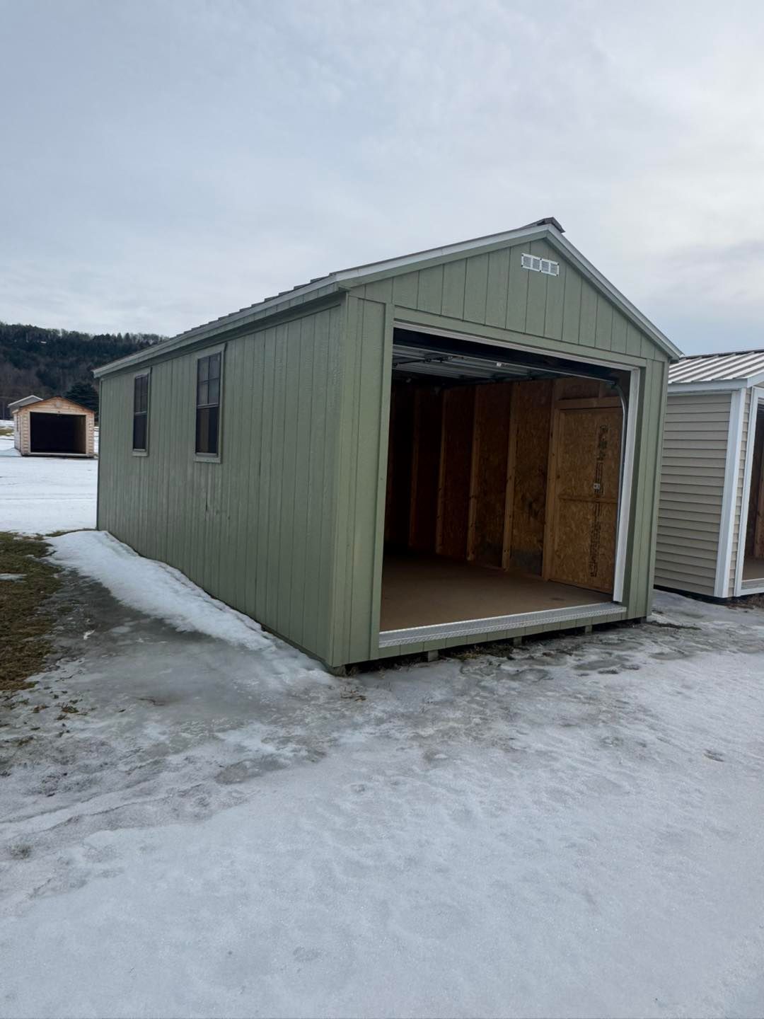 A green shed with a garage door is sitting in the snow.