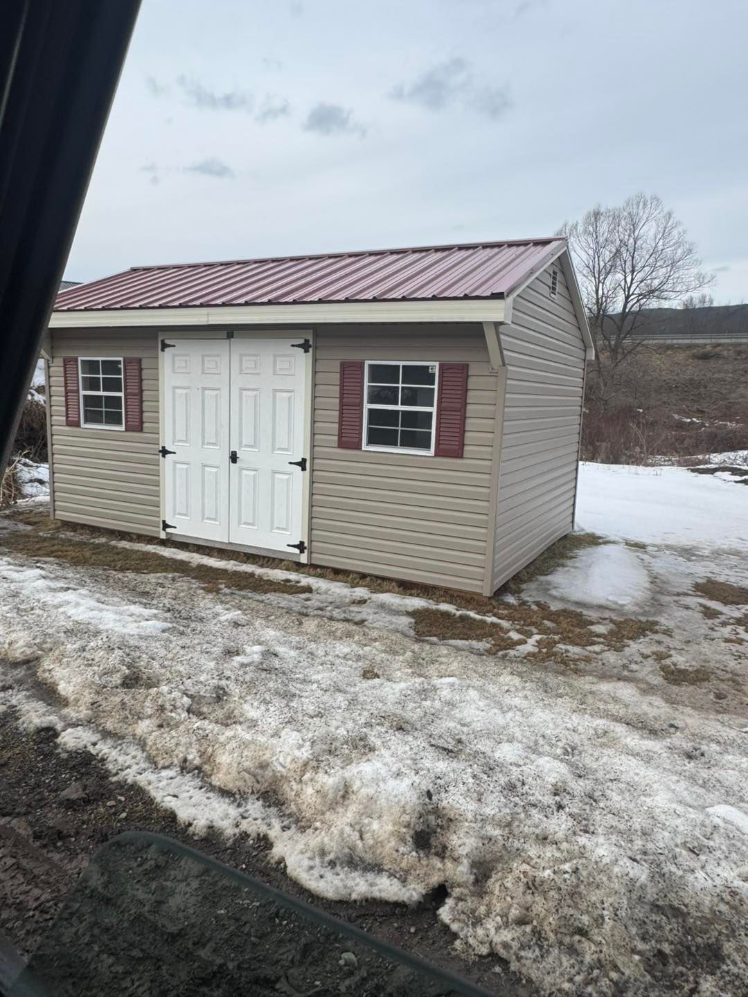 A small shed with a red roof is sitting in the middle of a snowy field.