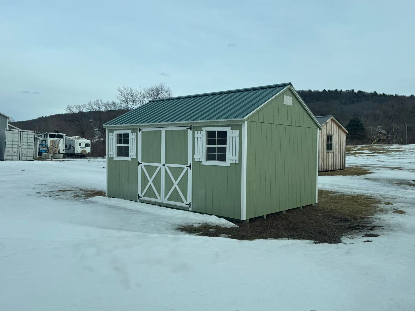 A green shed with a green roof is sitting in the middle of a snowy field.