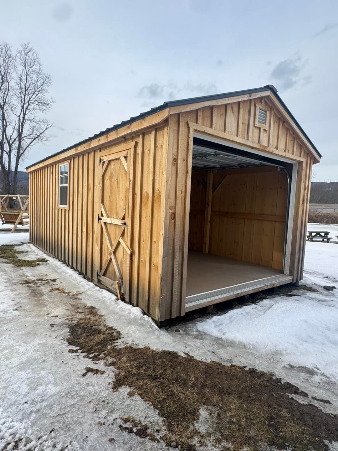 A wooden garage with the door open in the snow.