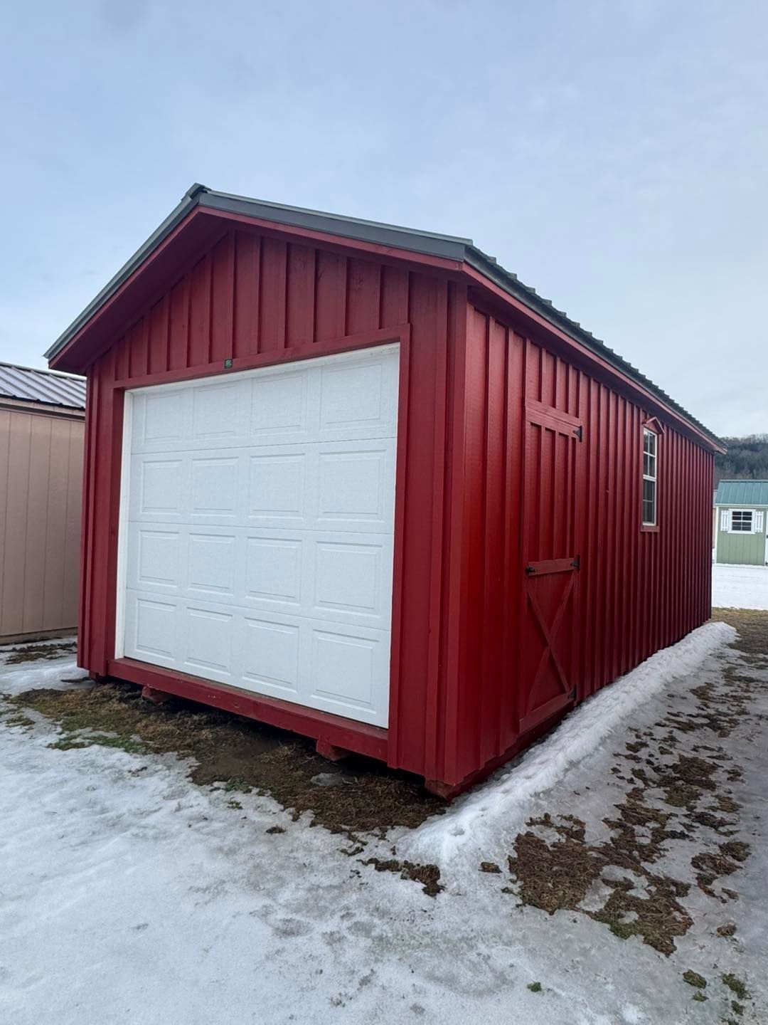 A red garage with a white garage door is sitting in the snow.