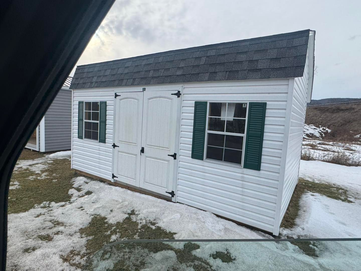 A white shed with green shutters is sitting in the snow.