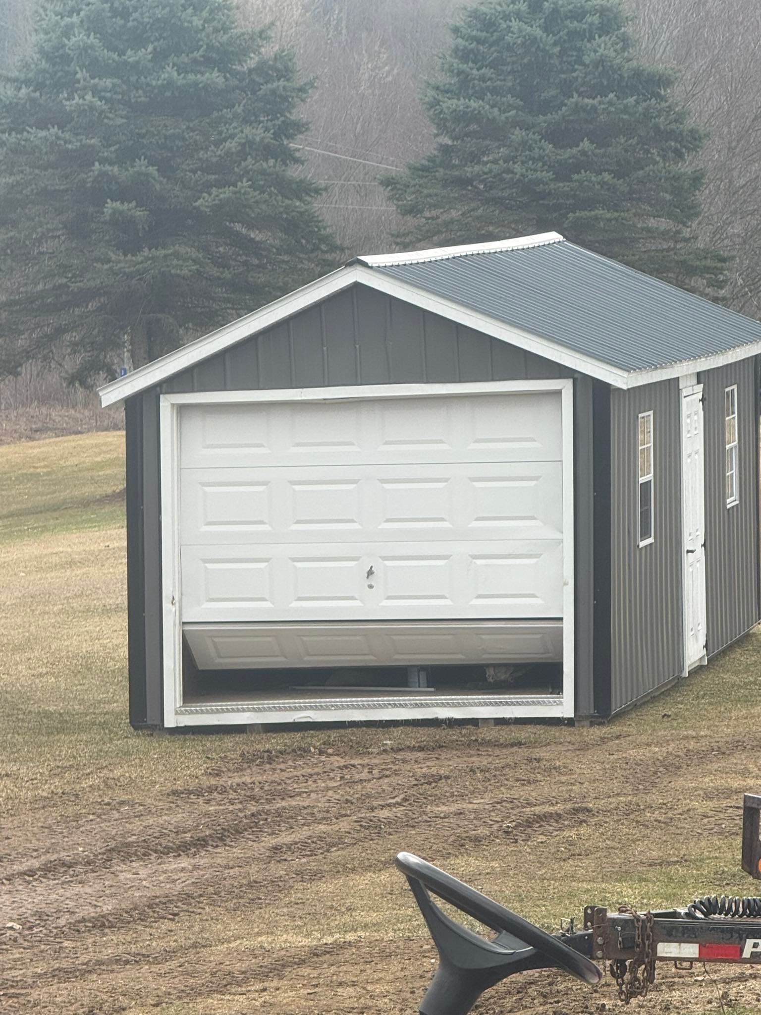 A shed with a garage door open in a field.