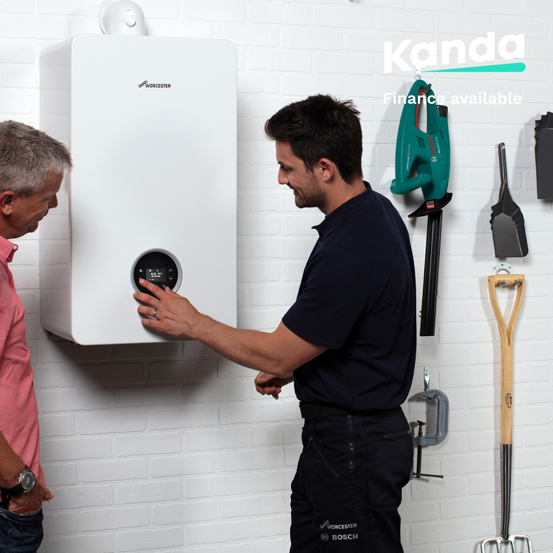 Two men are standing next to each other in front of a boiler.