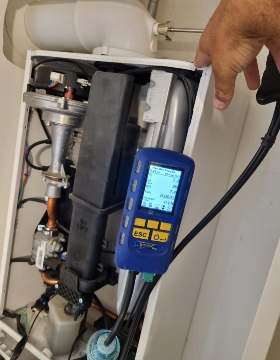 A person is holding a blue device in front of a boiler.