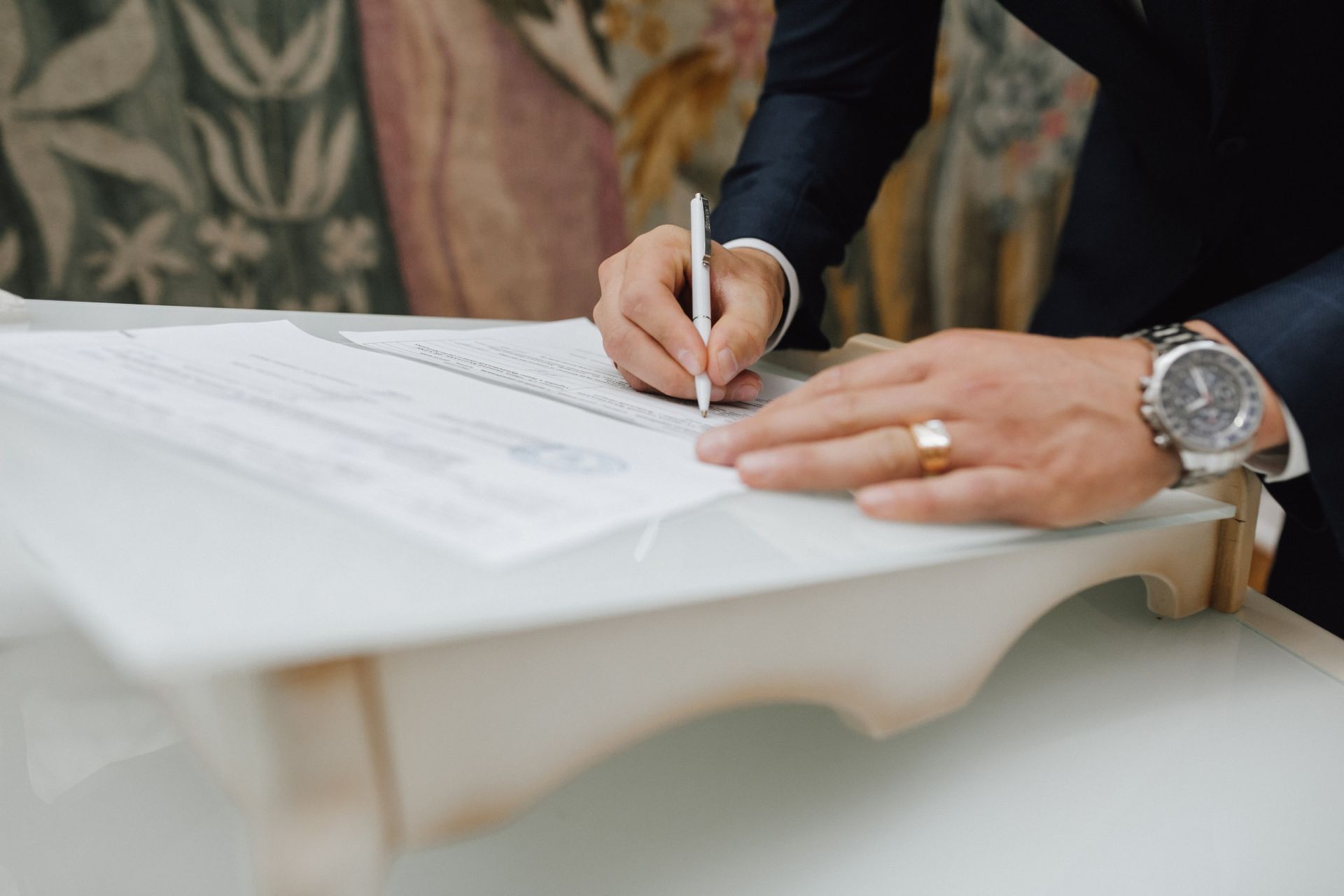 A man in a suit is signing a document with a pen.