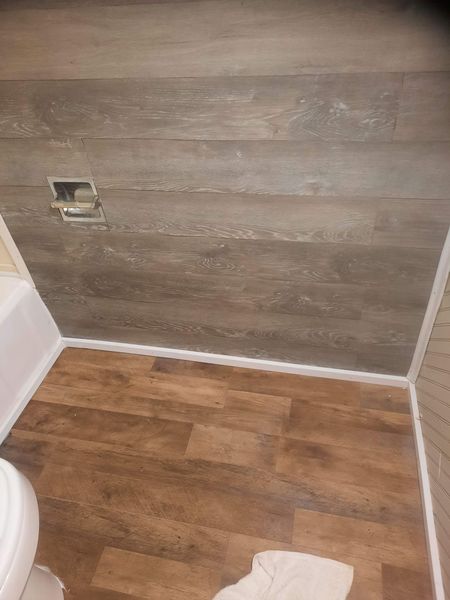 Bathroom with wood-look paneling and flooring. A white toilet is visible. White caulk seals the edges.