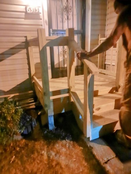 Person building wooden steps with handrail outside a house at night.